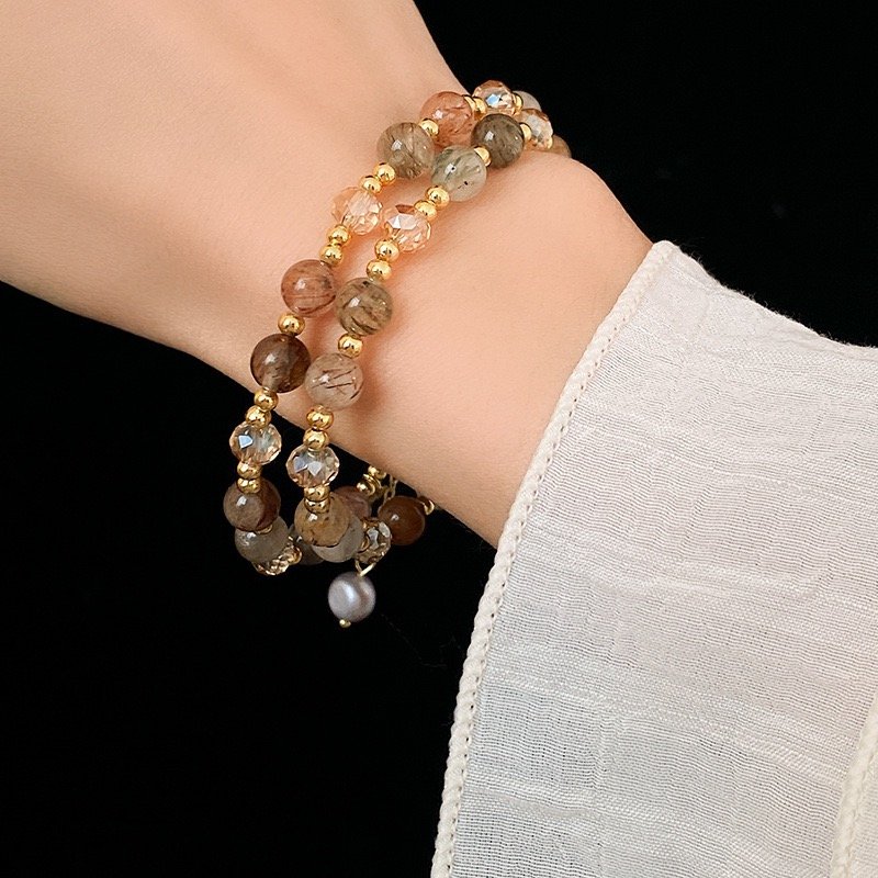 Layered natural stone beaded bracelet worn on wrist with gold-tone charm